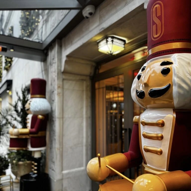 Large red and gold nutcracker soldier statues at luxury hotel entrance during Christmas season.