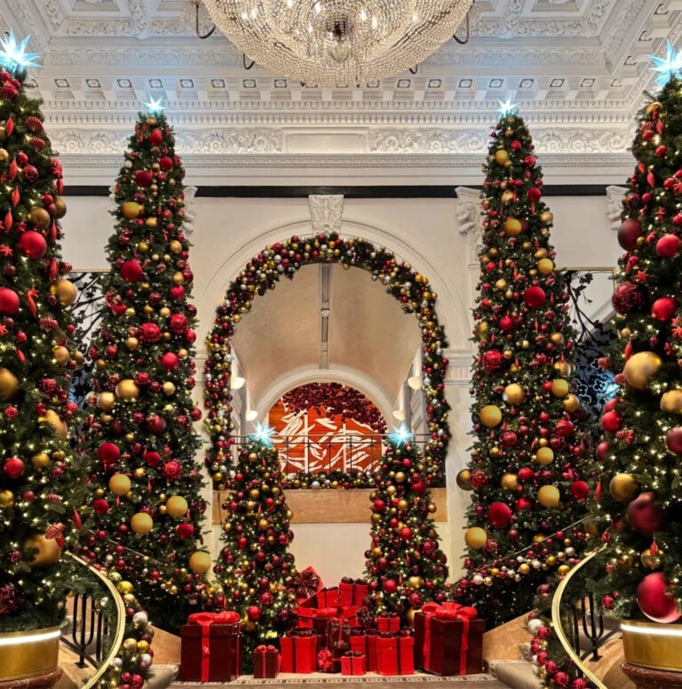 Opulent staircase decorated with red and gold Christmas trees and wrapped gifts.