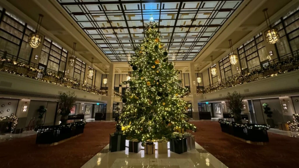 Book grand hotel lobby Christmas tree decoration with luxury lights and wrapped gift boxes.
