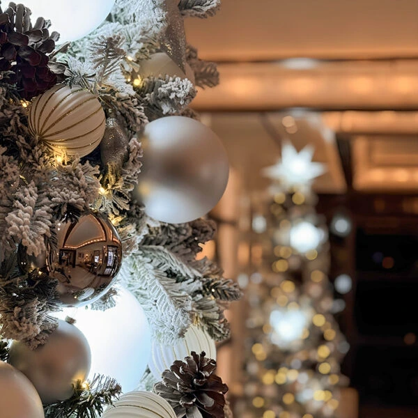 Close-up of snowy Christmas tree branches with silver and white ornaments.